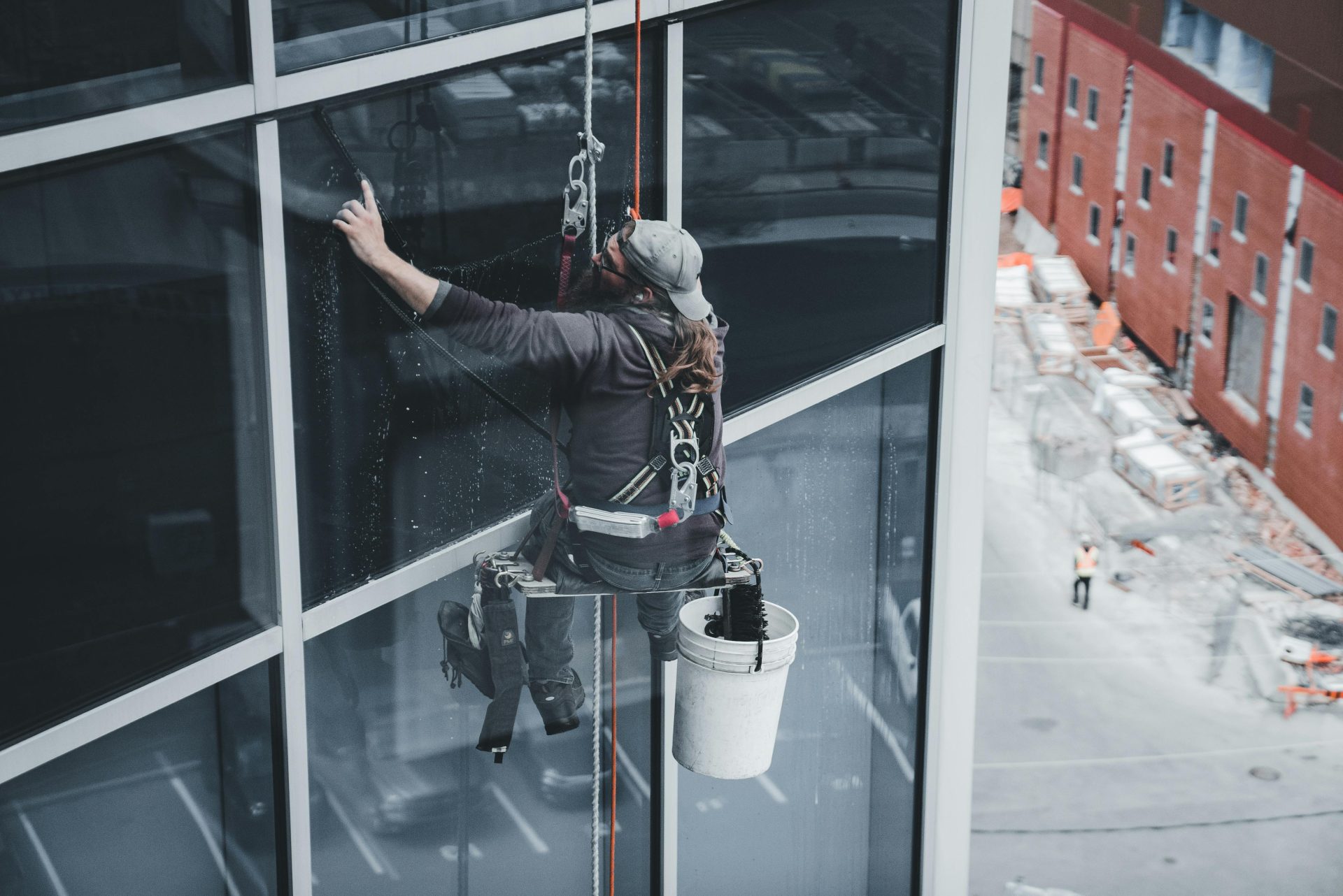 Ein Arbeiter reinigt mit einem Sicherheitsgurt die Fenster eines Wolkenkratzers in einer städtischen Umgebung.